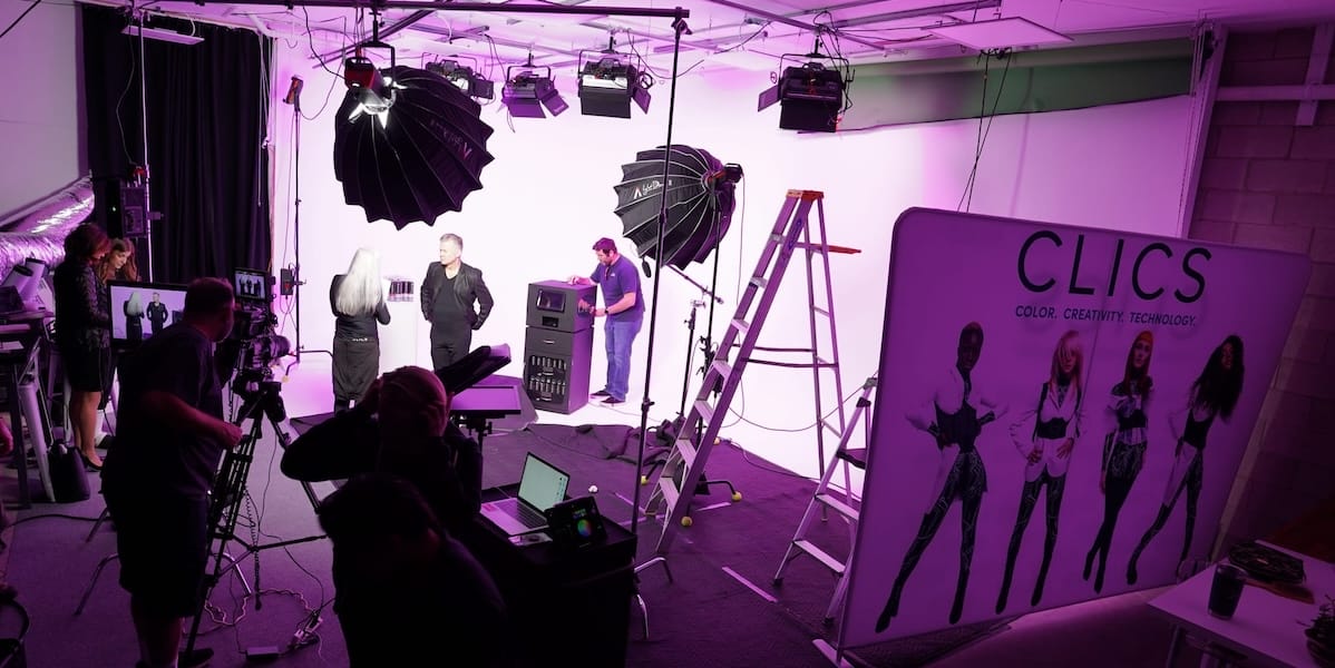 Photography shoot in progress at REV Studios with models on the cyc wall, professional lighting, and a production team, all under magenta lighting.